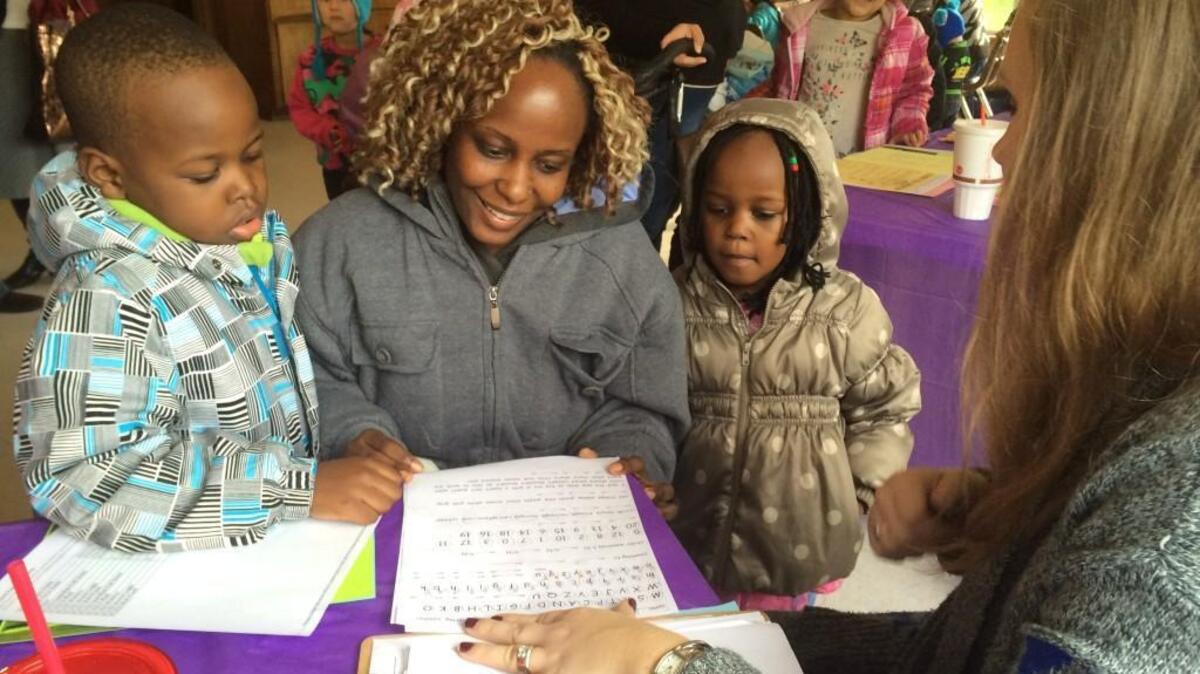 Mom Carolyne Waweru, center, smiles as she hears from teacher Annamarie Volz, right, that her son Marius is excelling in kindergarten at Park Lodge Elementary. Little sister Madlyn, right, seems interested, too.