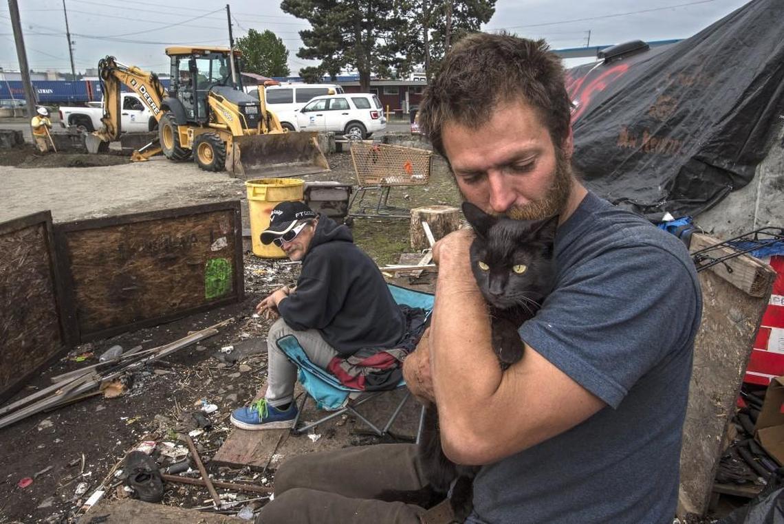 Anthony Laird, right, homeless for five years, comforts his cat as backhoes finish a trench Friday that will bring water to the large homeless encampment he and more than 50 others have been living in near Portland Avenue and 18th Street East on the Tideflats.