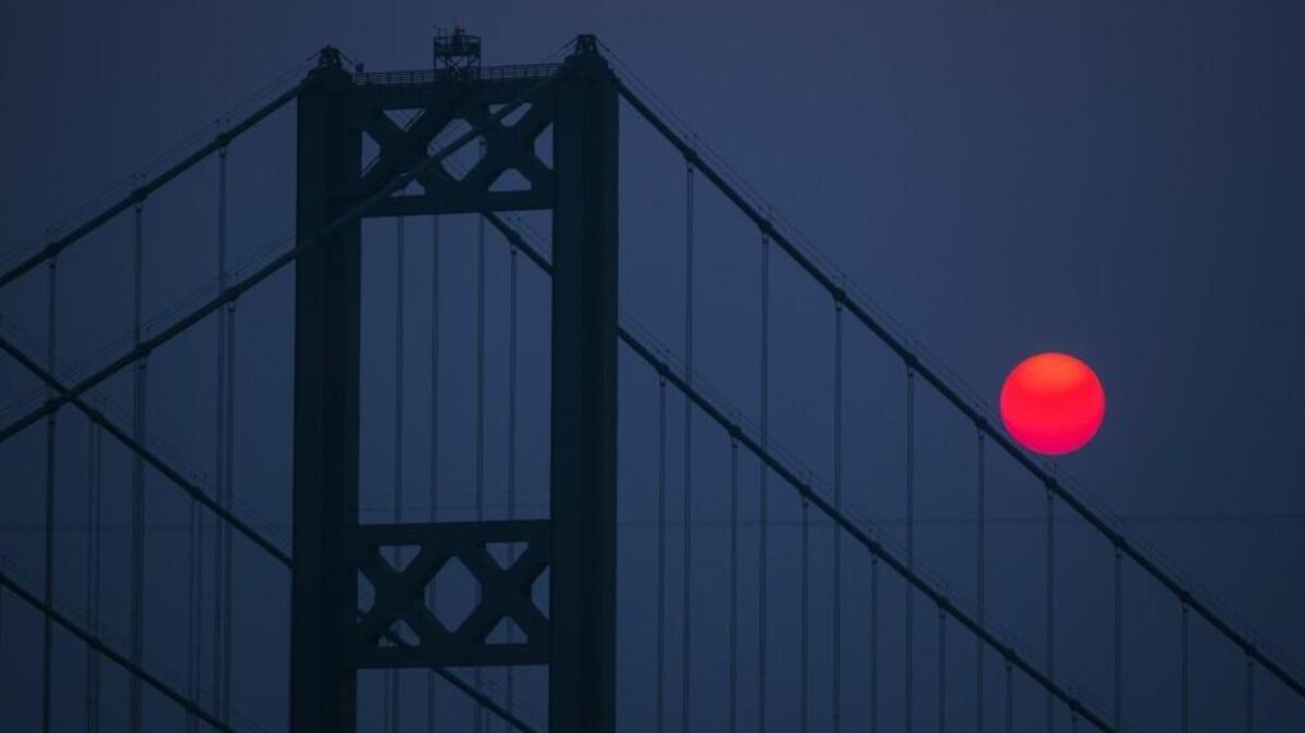 The sun sets behind the Tacoma Narrows Bridge. Smoke from wildfires in Canada are creating a haze throughout Tacoma.