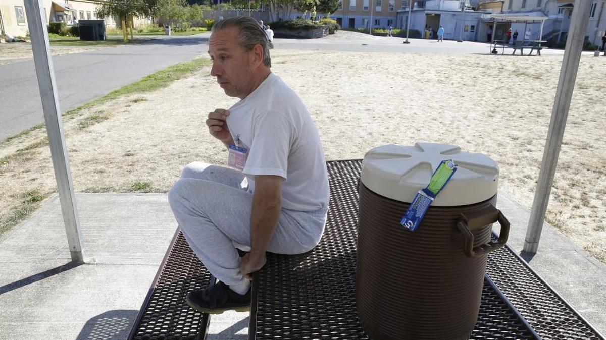 J.D. McManus, who has lived at the Special Commitment Center on McNeil Island since 2001, sits next to a cooler of drinking water in a recreation yard and talks about how his shirts turn brown after being laundered at the facility.