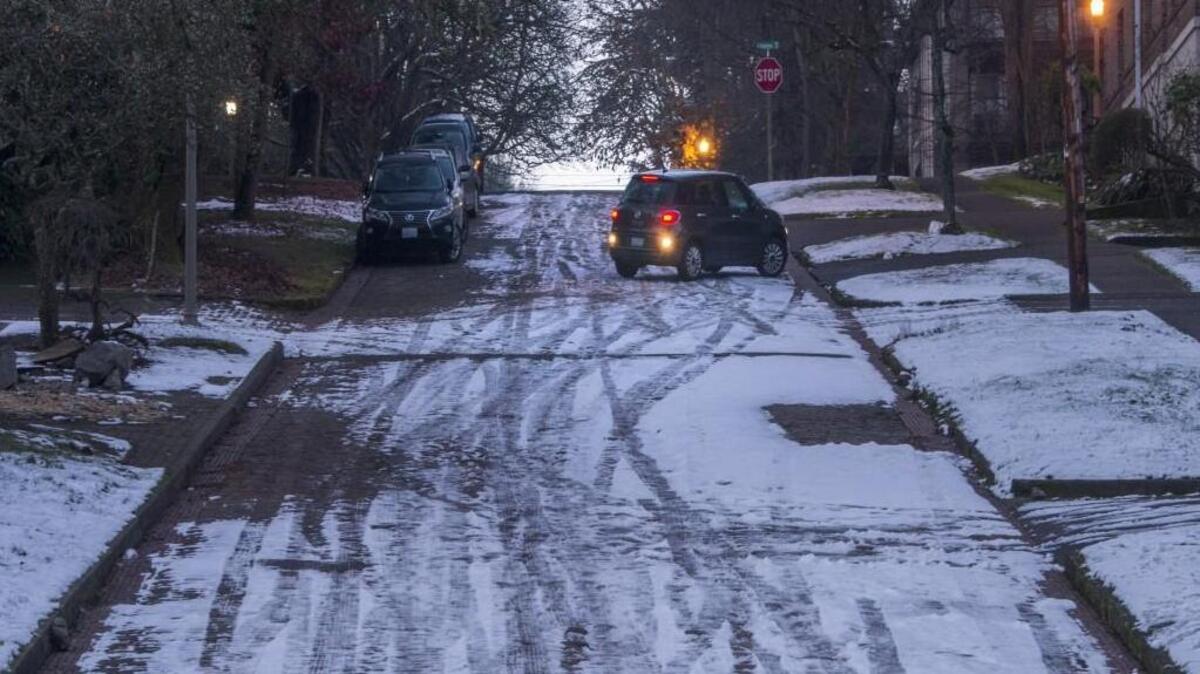 A car carefully pulls onto a steep ice- and snow-covered street in North Tacoma on Tuesday, December 26, 2017.