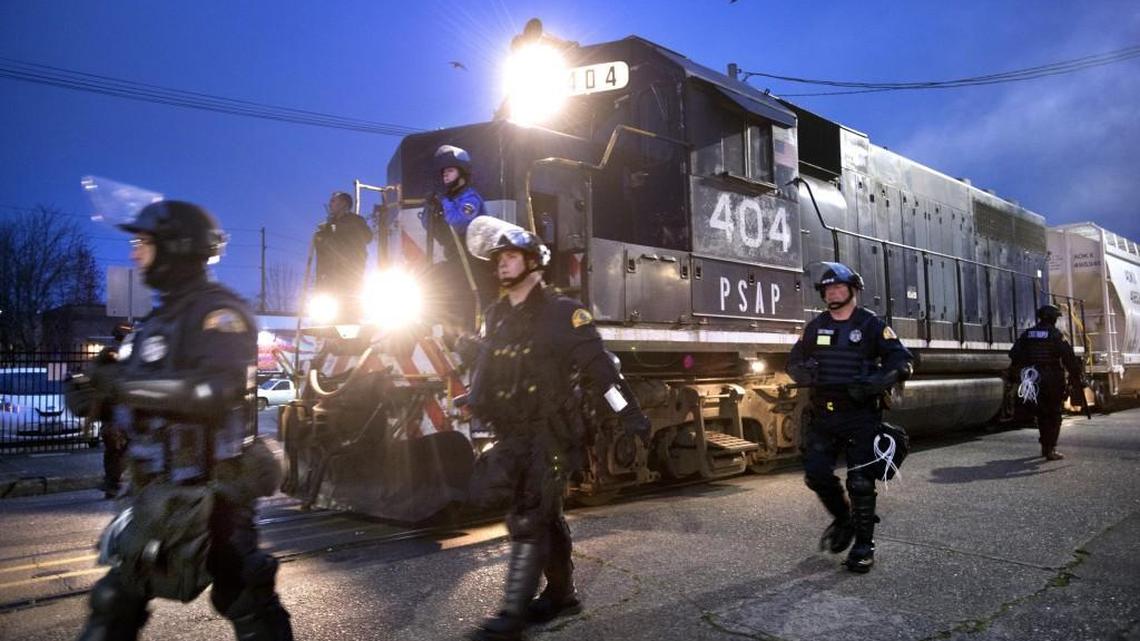 Law enforcement officers escort a train carrying ceramic proppants as it moves from the Port of Olympia through downtown early Friday.