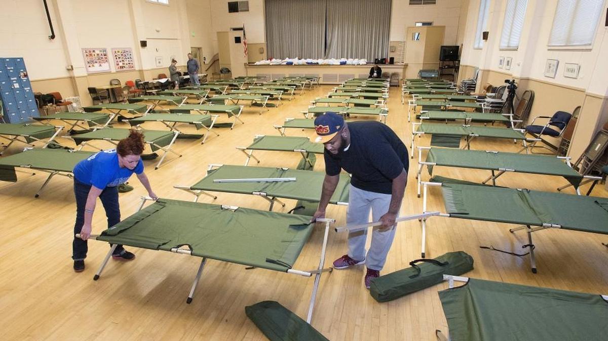 Omar Rashid, right, an outreach worker with Community Youth Services, and volunteer Linda Rick help set up about 40 cots for a cold-weather shelter at Beacon Senior Center in Tacoma on Monday, Dec. 14, 2015, for people ages 18-24 who experiencing homelessness.
