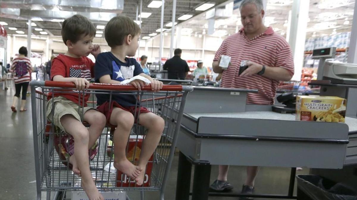 In this June 4, 2014 photo, Patrick Faye, right, looks at a receipt after making a purchase with his twin sons Sean, left, and Ryan, at a Costco in Plano, Texas.