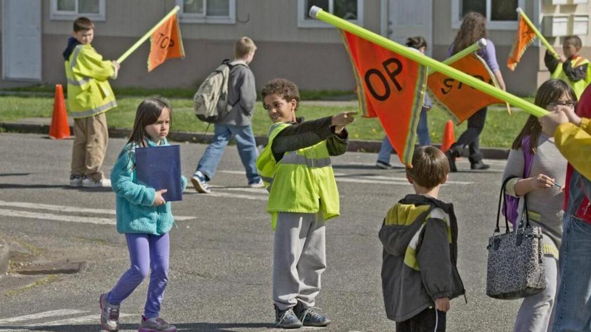 Third grader crossing guard Marquis Trimble enthusiastically assists Lorenne Mendoza as she and others cross the street at Bryant Montessori in 2013.
