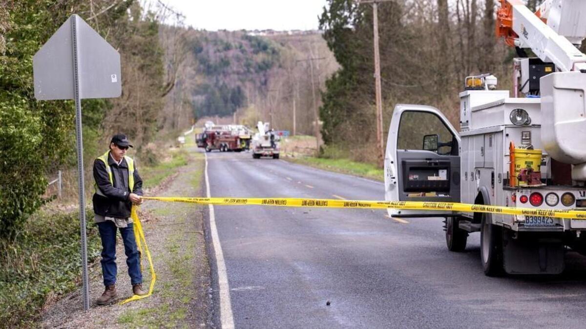 A Puget Sound Energy employee puts up caution tape while repairs are made on a downed power line on 96th Street East in Puyallup on Sunday.
