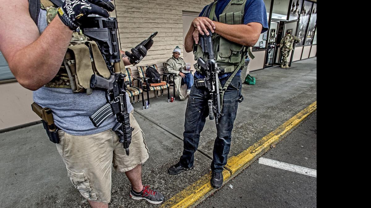 
Zach, 27, left, and his good friend Matt, 34, stand outside the U.S. Army Recruiting Office on 16204 Pacific Ave. South, Spanaway, carrying AR-15 rifles and holstered semiautomatic handguns. Zach said he called the office earlier in the morning to ask if it would be all right for them to come out. He said they are there because of the shooting at another recruiting office in Chattanooga, Tennessee, that left five service members dead. Deanna Rine, seated behind, said “it is all right with me that they are here posing for pictures with their guns.” Rine was just hanging out in front of the recruiting office.
