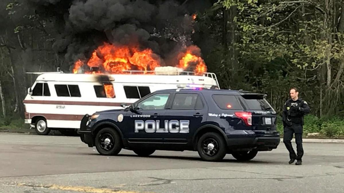 A Lakewood police officer stands near a flaming RV on Tuesday