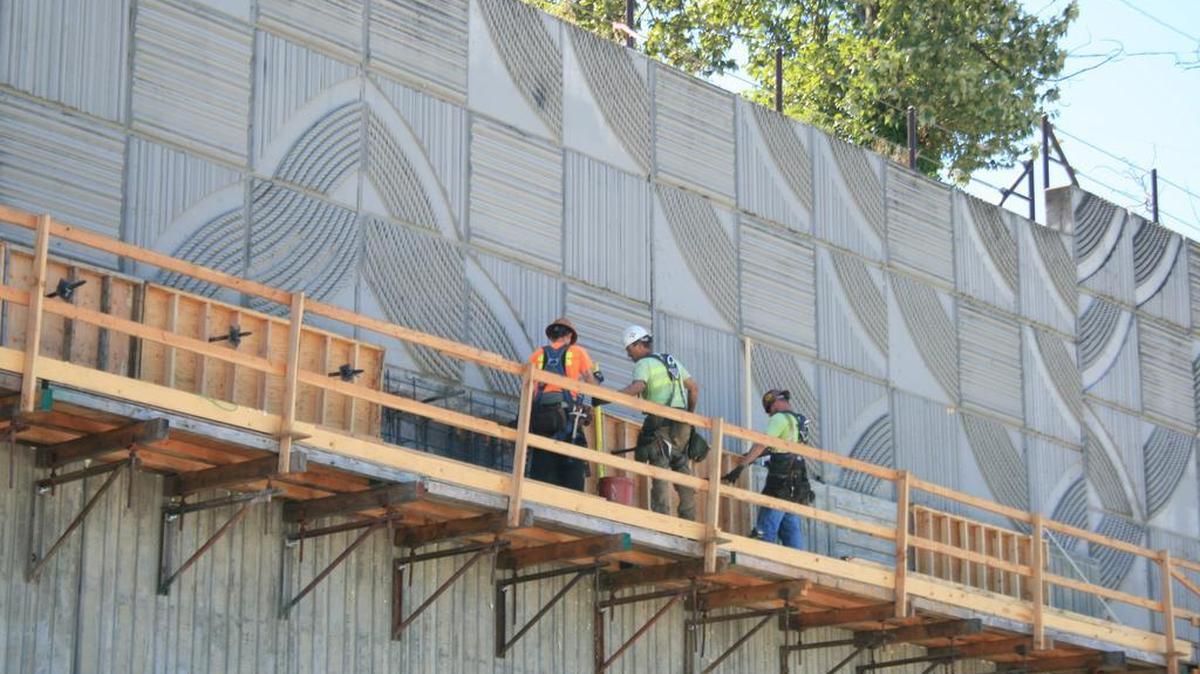 
Construction workers stand on scaffolding July 30 in front of Vicki Scuri’s public art on an Interstate 5 retaining wall in Tacoma. The work, called “The Great Wall,” is now abutted with a more conventional pattern used throughout the I-5 corridor.
