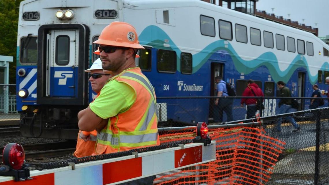 Constructions workers wait for a Sounder train to leave the Auburn station before resuming work early Tuesday. Crews hired by BNSF are adding a third track through the area.