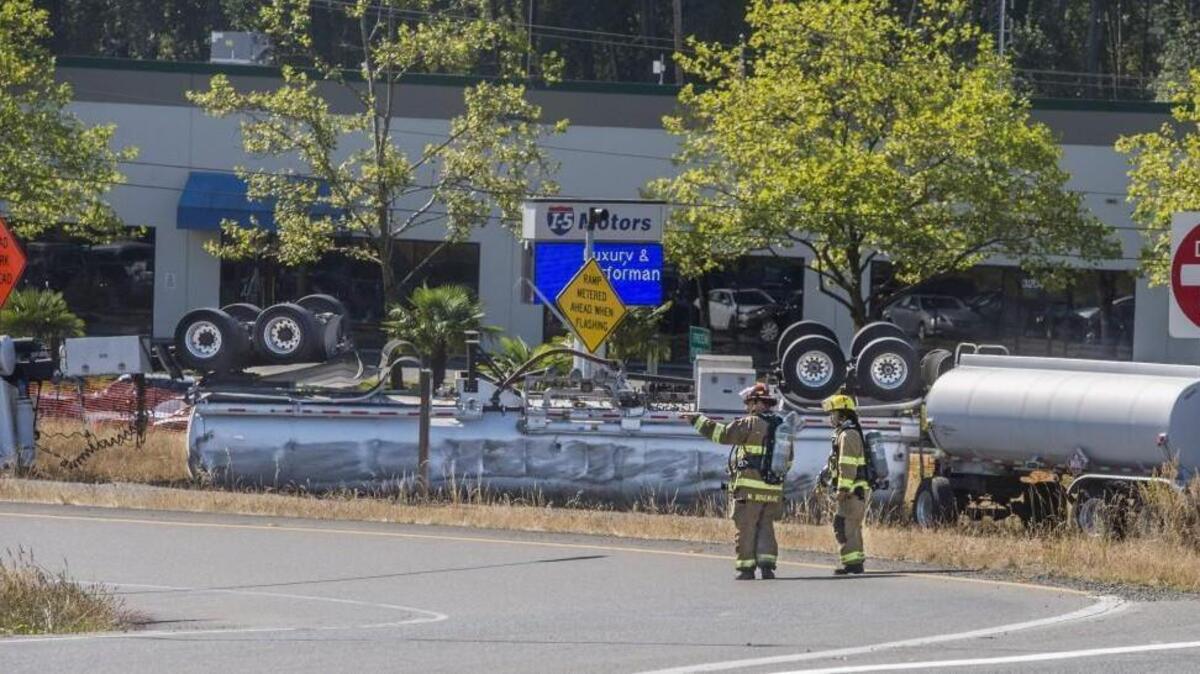 Firefighters stand near an overturned gas tanker at the Port of Tacoma Road entrance to Interstate 5, August 18, 2016. Both directions of the freeway were closed because of a large spill.