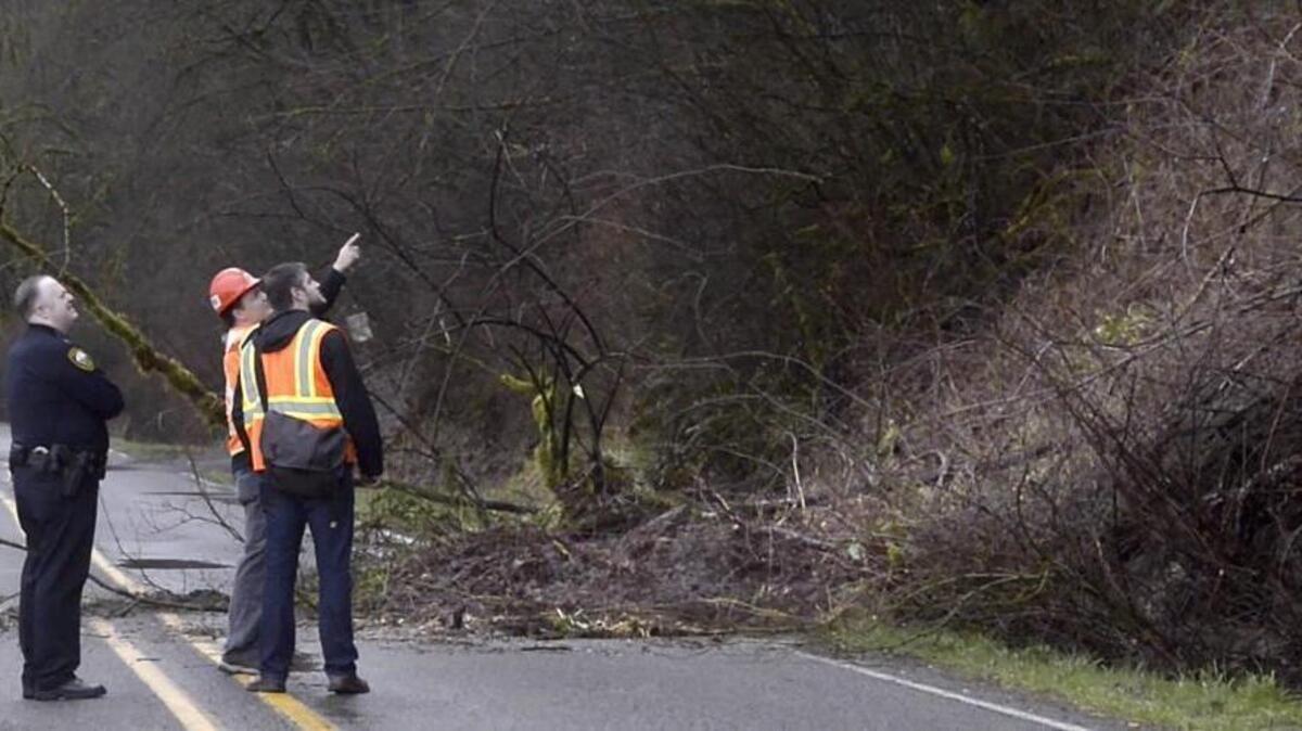 Puyallup Police Capt. Scott Engle, right, watches workmen inspect a landslide along East Pioneer Way in Puyallup on Thursday. The mudslide risk has prompted officials to close Pioneer Way in the 3400 block through Monday.