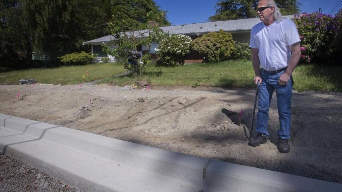 Dan Larson looks at the city putting a new sidewalk in front of his house on Elwood Drive West in University Place in early May. Larson wants to put in a new driveway because he has multiple sclerosis, needs a cane to get around and believes he'll be in a wheelchair in three years. The city initially said a hearing examiner would have to make an exception to allow the sidewalk, but after receiving an application from Larson approved his request administratively.