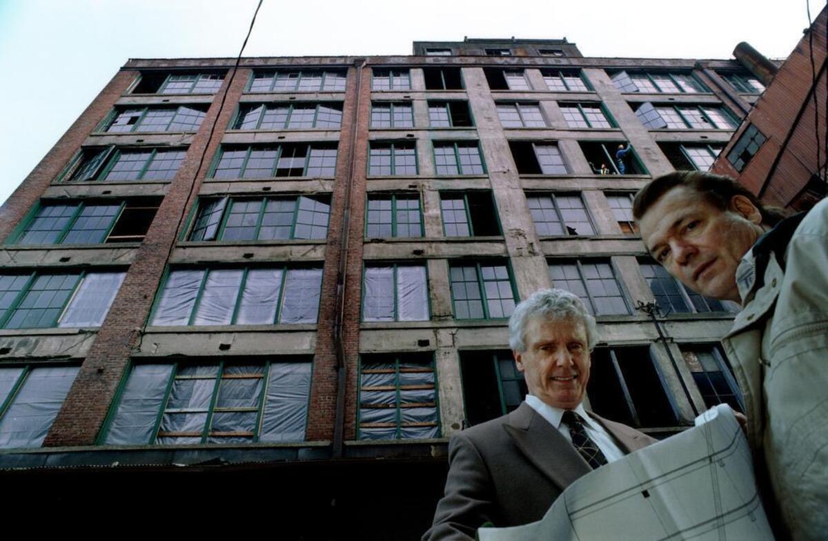 Fred Roberson and Gary Davis outside the old Harmon Warehouse building, which fronts Pacific Ave. Pictured is the back of the building off of Commerce St., showing workmen leaning out of a upper window as they paint the window frame.
