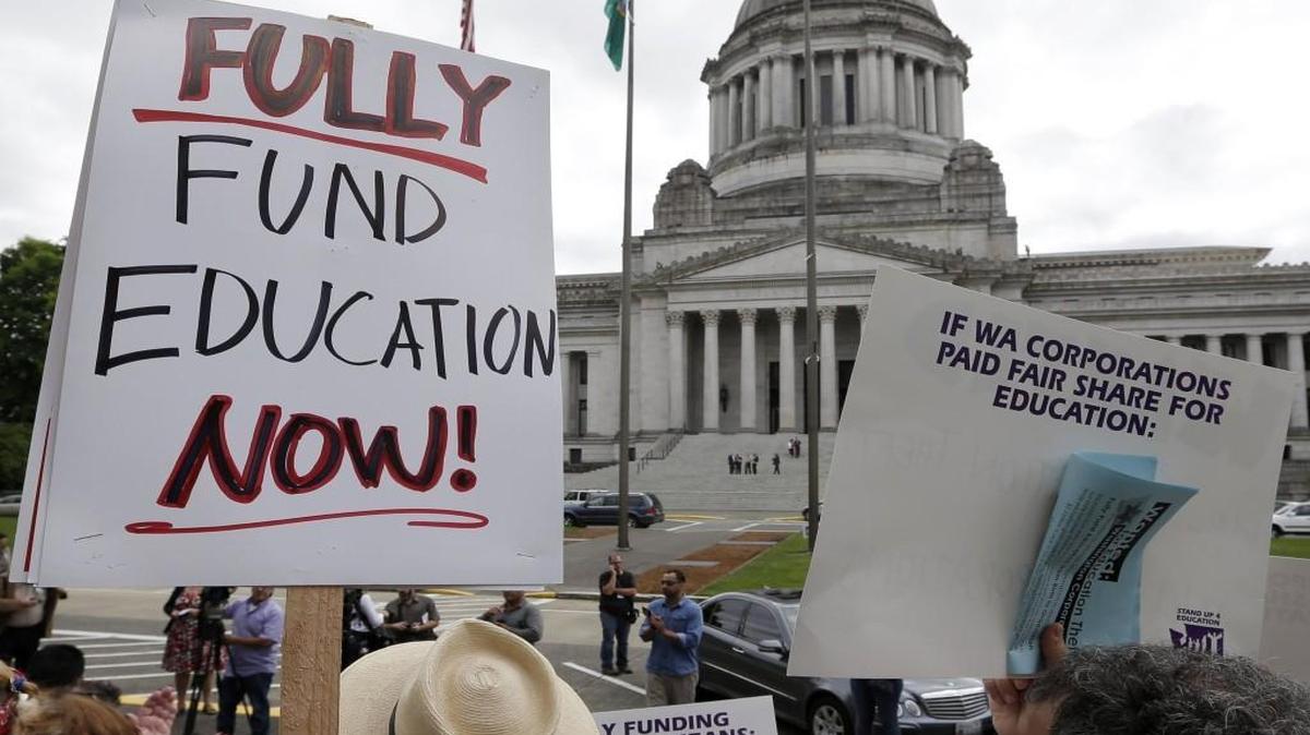 A small group of demonstrators stand on the steps of the Temple of Justice and in view of the Legislative Building as they advocate for more state spending on education prior to a hearing before the state Supreme Court Wednesday, Sept. 3, 2014, in Olympia.