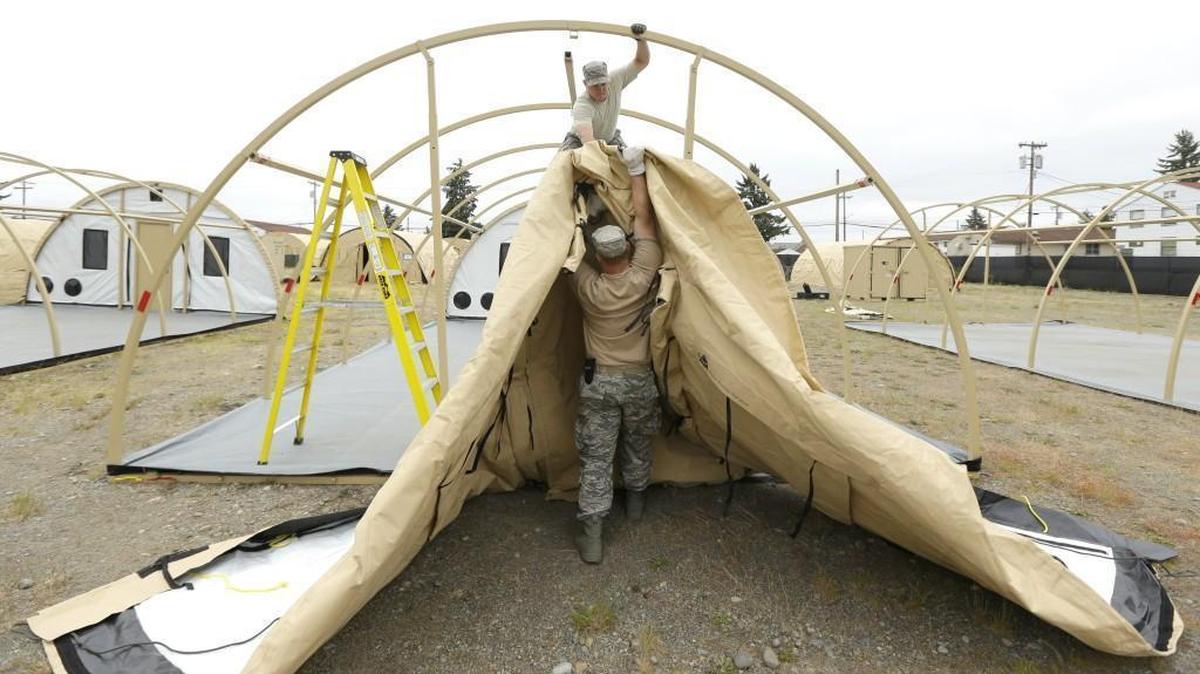 Washington Air National Guard Staff Sgt. Andrew Waddell, top, and Master Sgt. Tyler Bates, bottom, work to assemble temporary living structures at Joint Base Lewis-McChord that will be used by troops taking part in a massive earthquake and tsunami readiness drill overseen by the Federal Emergency Management Agency next week.
