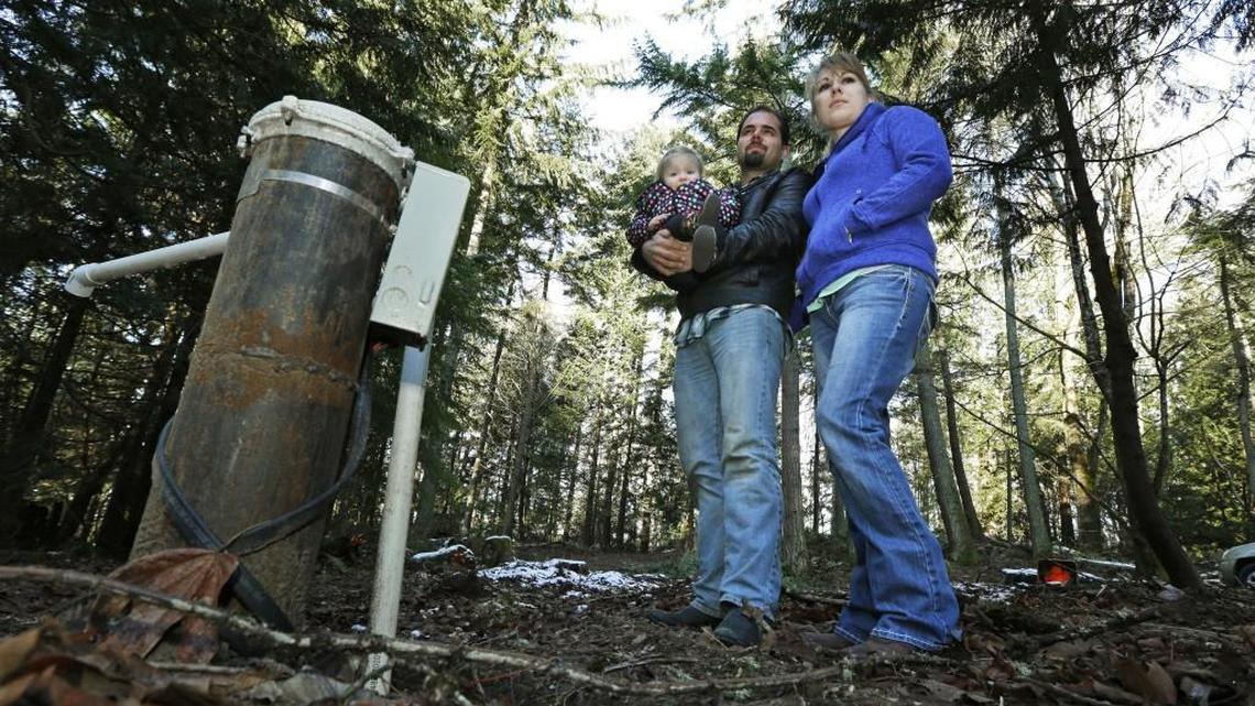 FILE - In this Dec. 6, 2016 file photo, Bud Breakey and his wife Deborah pose for a photo with their daughter Kaylin, 15 mos., by the water well they paid to drill on property they own near Bellingham, Wash. where they hope to eventually build a house. Lawmakers are tangling over legislation to address a recent Washington Supreme Court decision that put the onus on counties to determine whether water is legally available in certain rural areas before they issue building permits. (AP Photo/Ted S. Warren, file)