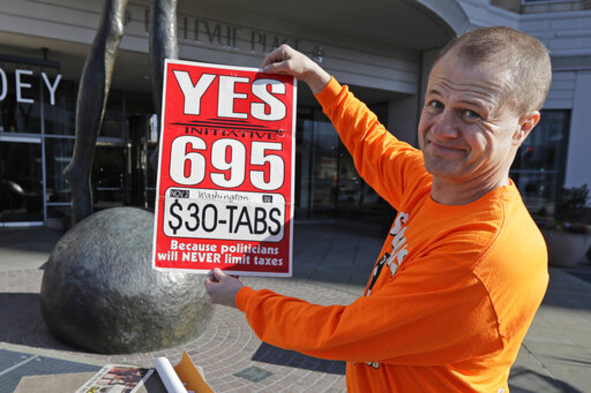 Anti-tax activist Tim Eyman poses for a photo with a sign from his original 1999 campaign for $30 car registration tabs, as he waved a sign for his current Initiative 976 on election day in Bellevue.