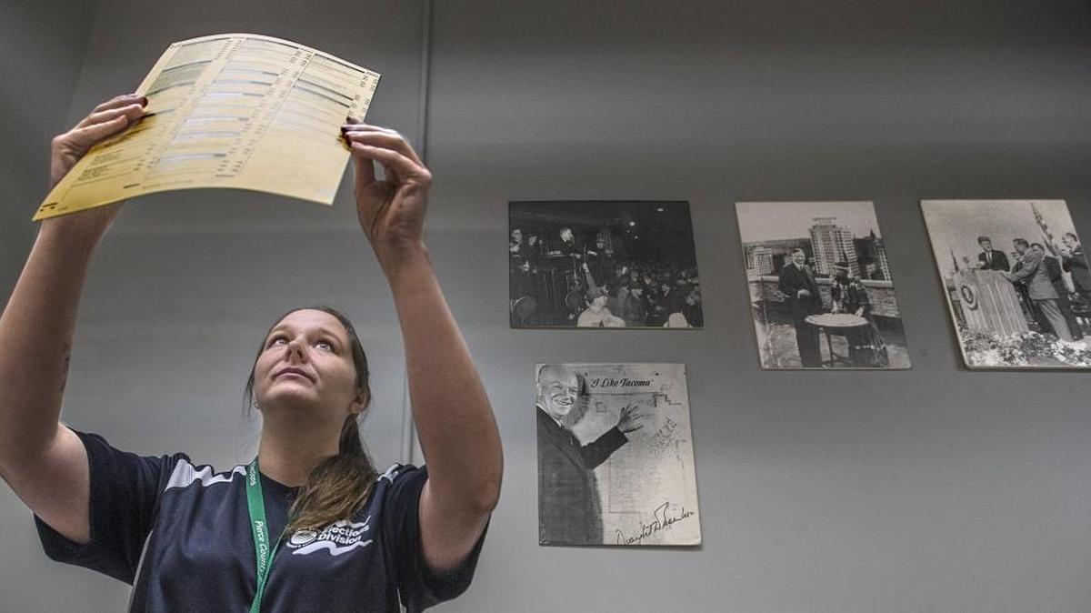 Jennifer Andre examines newly printed ballots used in remaking ones that contained errors and would not have been counted correctly. On the wall behind Andre at the Pierce County Elections Center are historical photographs showing presidential visits to Tacoma by Franklin D. Roosevelt, Dwight D. Eisenhower and John F. Kennedy.