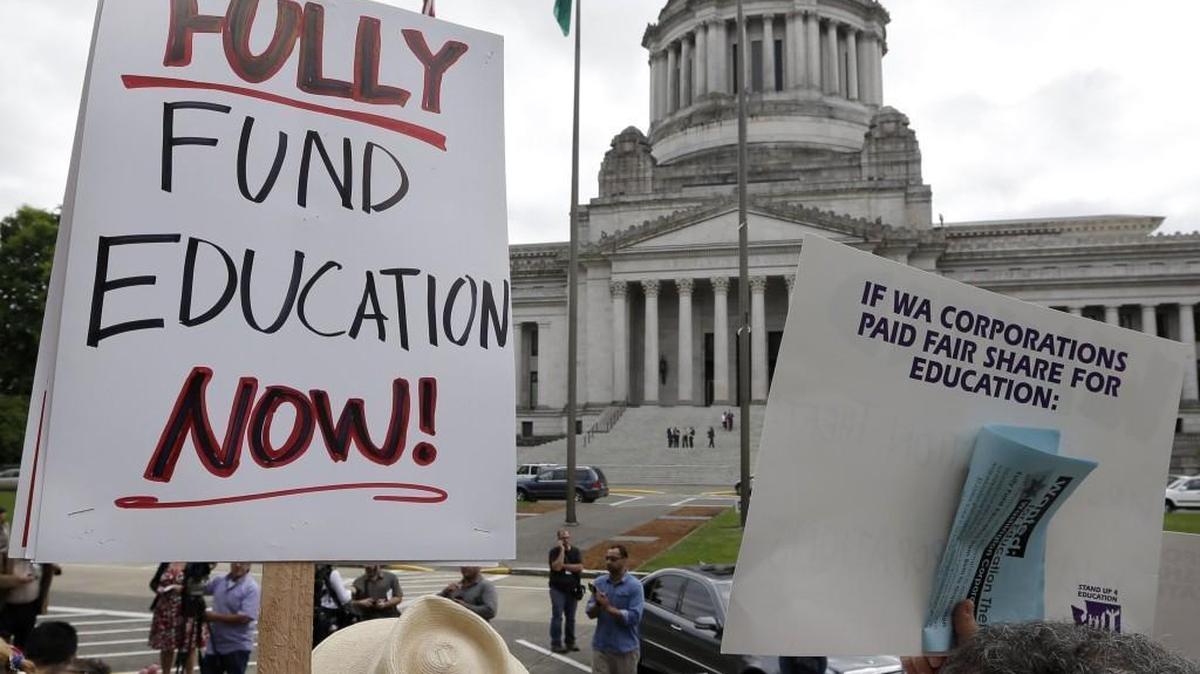 A small group of demonstrators stand on the steps of the Temple of Justice and in view of the Legislative Building as they advocate for more state spending on education prior to a hearing before the state Supreme Court Wednesday, Sept. 3, 2014, in Olympia, Wash. (AP Photo/Elaine Thompson)