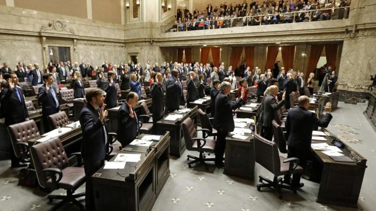 Washington state representatives take part in a group swearing-in, Monday, opening day of the legislative session at the Capitol in Olympia.