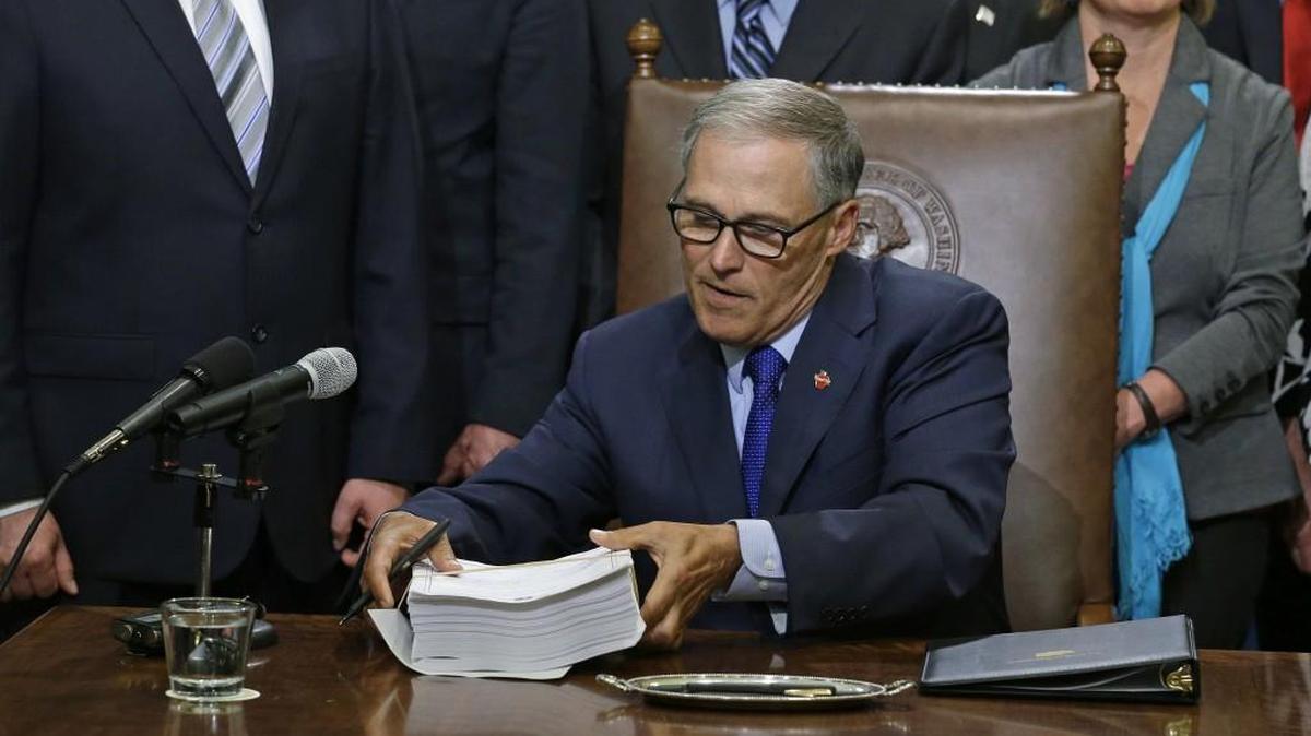 Washington Gov. Jay Inslee lifts a copy of the new two-year state operating budget before signing it Friday, June 30, 2017, at the Capitol in Olympia, Wash. The budget was approved by the Legislature earlier in the day, just in time to avert a partial government shutdown. (AP Photo/Ted S. Warren)