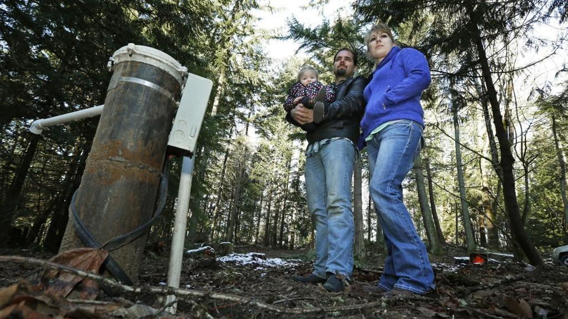 FILE - In this Dec. 6, 2016 file photo, Bud Breakey and his wife Deborah pose for a photo with their daughter Kaylin, 15 mos., by the water well they paid to drill on property they own near Bellingham, Wash. where they hope to eventually build a house. Lawmakers say they have reached a deal to address a recent Washington Supreme Court decision that put the onus on counties to determine whether water is legally available in certain rural areas before they issue building permits. (AP Photo/Ted S. Warren, file)