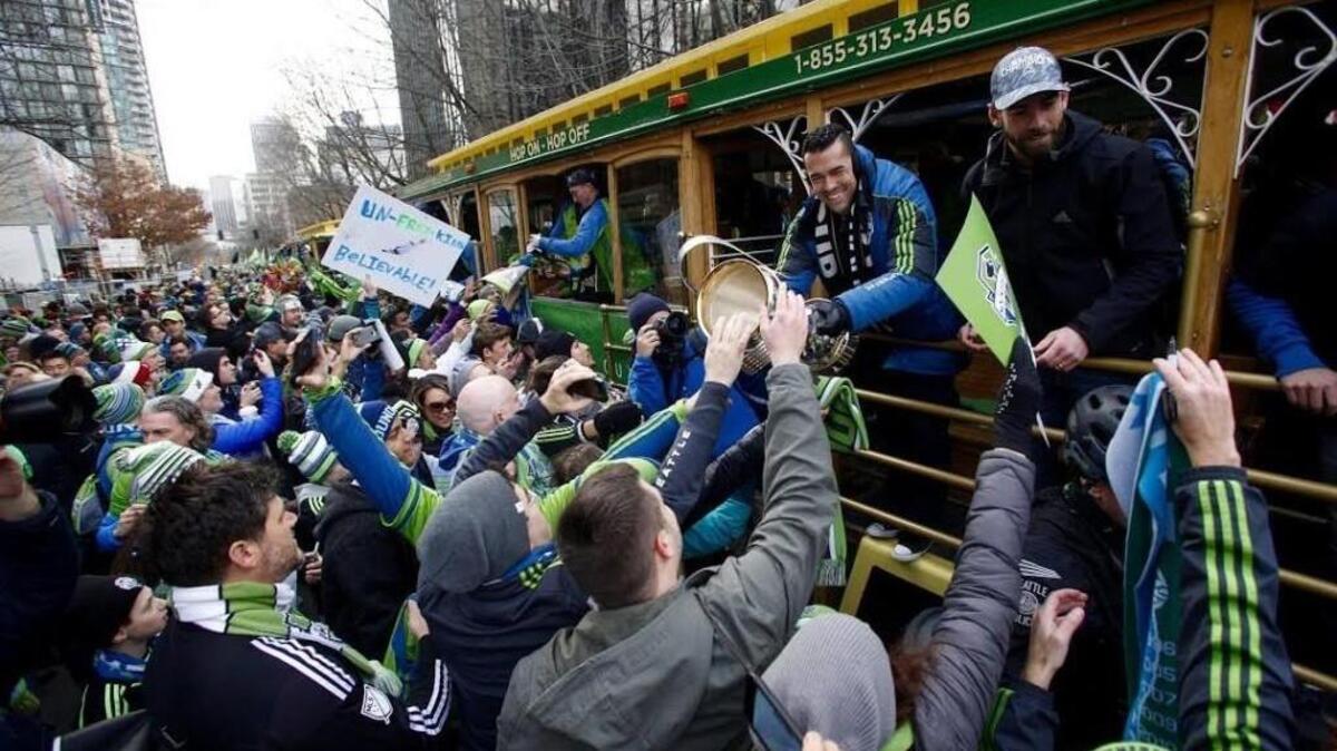 Sounders players Herculez Gomez (left, holding trophy) and Zach Scott greet fans vying to touch the trophy during a Sounders parade and rally to celebrate their first MLS Cup victory in downtown Seattle on Tuesday.