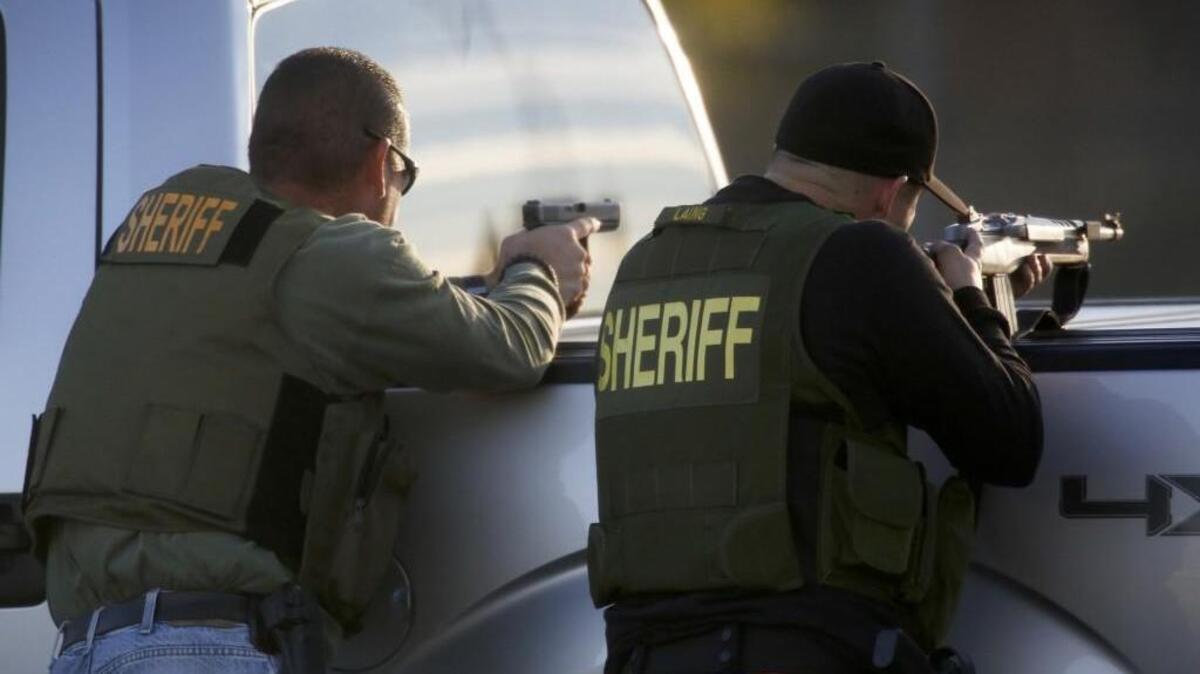 San Bernardino Sheriff’s deputies draw guns and take cover during an active search for the suspects involved in the mass shooting of 14 people at the Inland Regional Center in San Bernardino, Calif., on Wednesday.