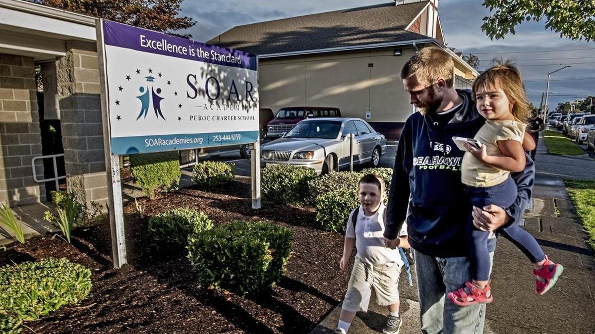 Greg Allman, carrying 2-year-old daughter Genevieve, walks his son Liam, 5, to the SOAR Academy, one of three charter schools that opened last year in Tacoma.