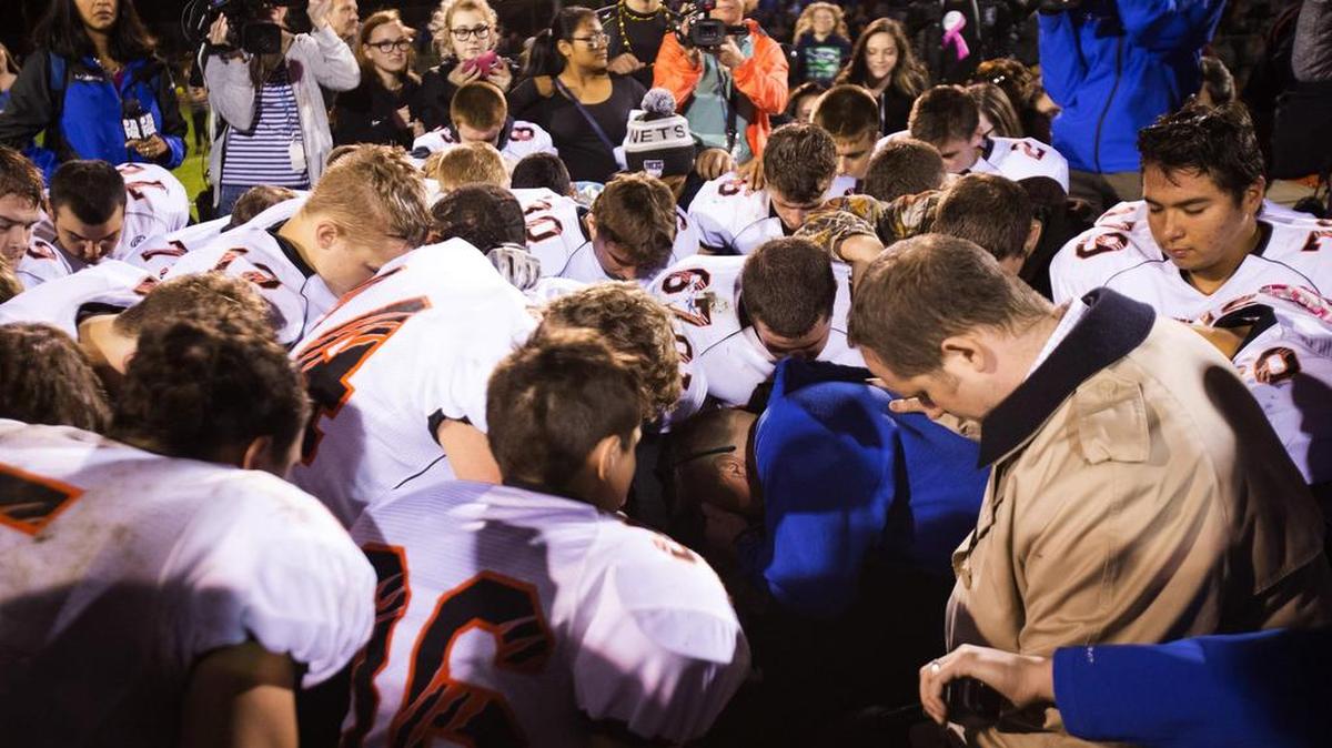 Bremerton High assistant football coach Joe Kennedy, center in blue, kneels and prays with his team Oct. 16.