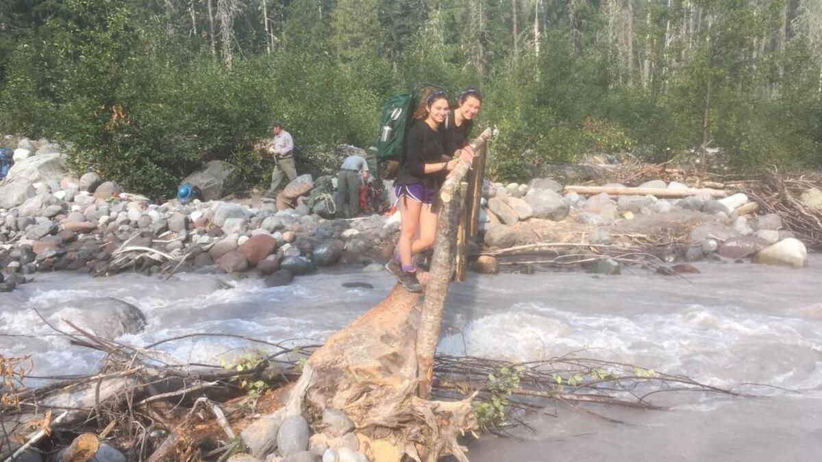 Along the west fork of the White River in Mount Rainier National Park, where a hiker was swept away and died last month, Noelle and Madeleine Misterek (from left) are glad to use a footbridge just completed by a trail crew (seen in background).