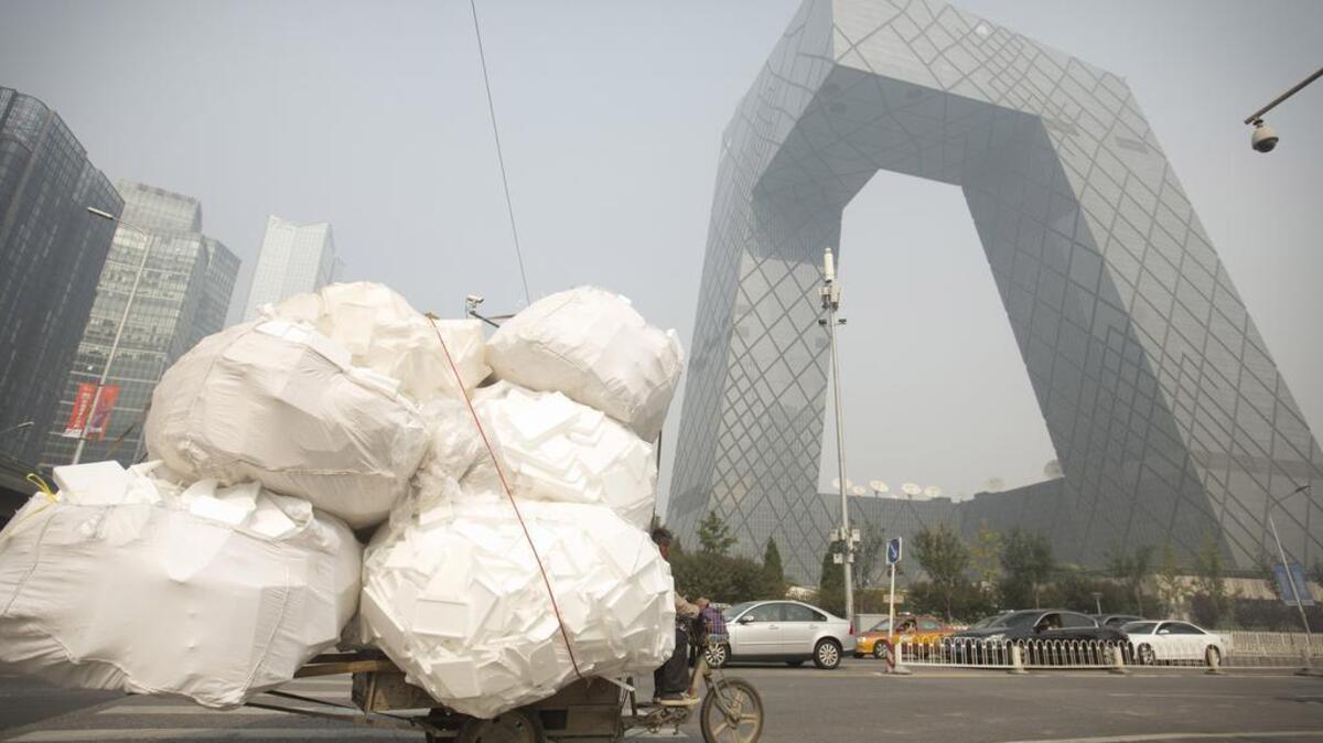 
A man on an electric cart carrying a load of styrofoam drives past the China Central Television headquarters building Oct. on a polluted day in Beijing.
