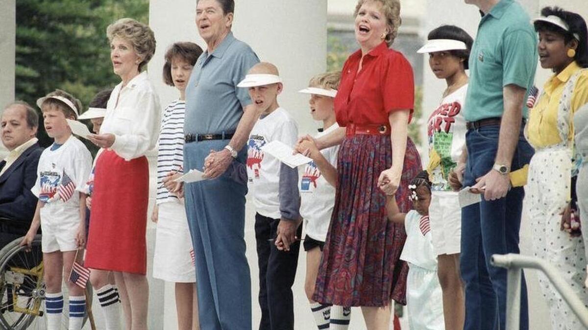 U.S. President Ronald Reagan and First Lady Nancy Reagan, joined by daughter Maureen and children of White House staff, clasp hands and sing during the Hands Across America line in front of the White House on May 25, 1986.