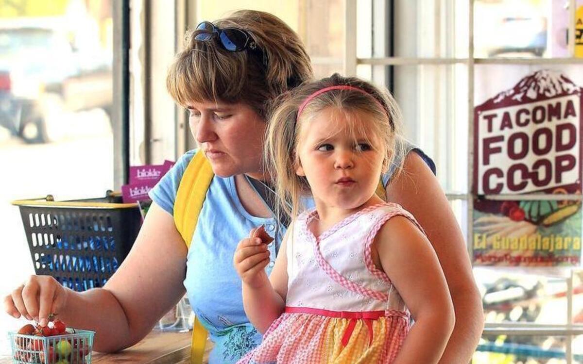 Cerridwen Chansley, 3, of Tacoma enjoys an organic cherry tomato while sitting on her mom Christine's lap at the Tacoma Food Co-op.