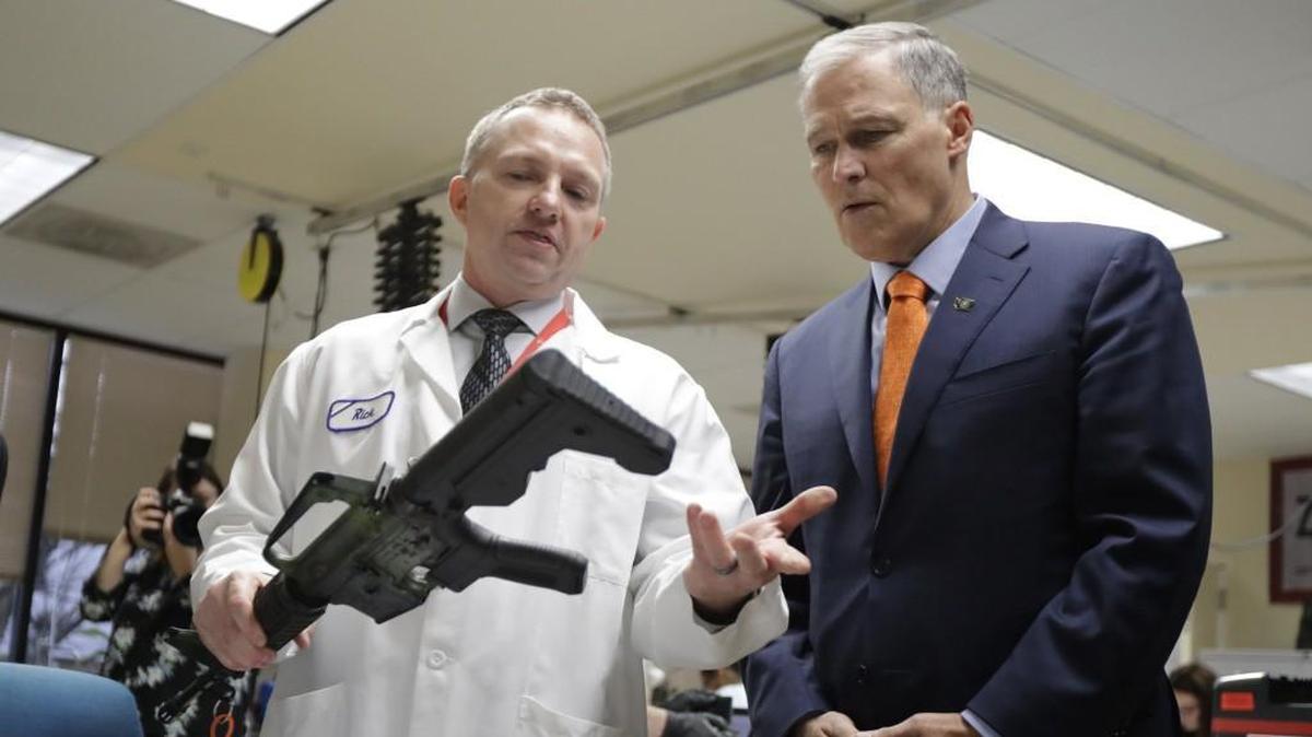 Gov. Jay Inslee talks with Rick Wyant, supervisor of the forensic firearms unit at the Washington State Patrol crime laboratory in Seattle, as Wyant holds a semi-automatic rifle fitted with a "bump stock" device to make it fire faster. Inslee has called for a ban on bump stocks. A Senate committee voted in favor of the ban last week.
