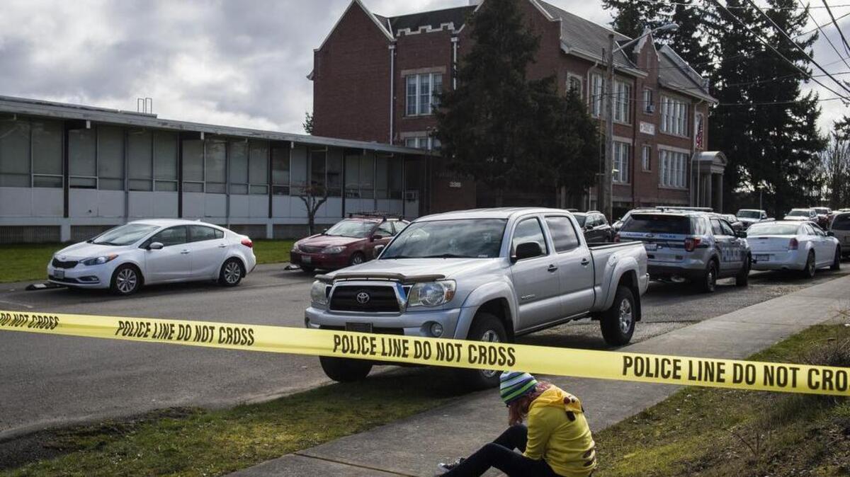 A student sits in the grass across the street as officers respond to reports of a shot fired at Oakland High School in Tacoma last year.