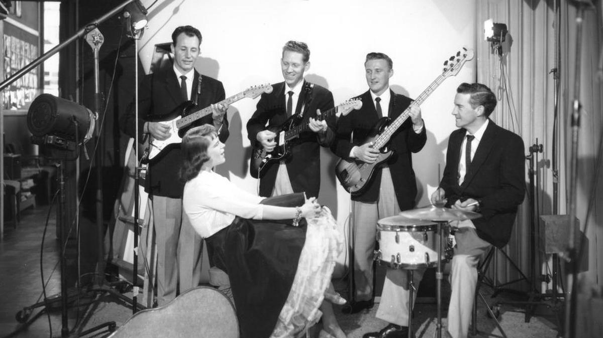In April 1960, the Tacoma-originated rock group “The Ventures” posed for a publicity photo with an unidentified woman admirer. (Left to right: Nole F. (Nokie) Edwards, Bob Bogle, Don Wilson, Howie Johnson.) The most popular and influential instrumental rock band of all time got its start playing at the Blue Moon in Tacoma. The Ventures were inducted into the Rock and Roll Hall of Fame in March 2008.