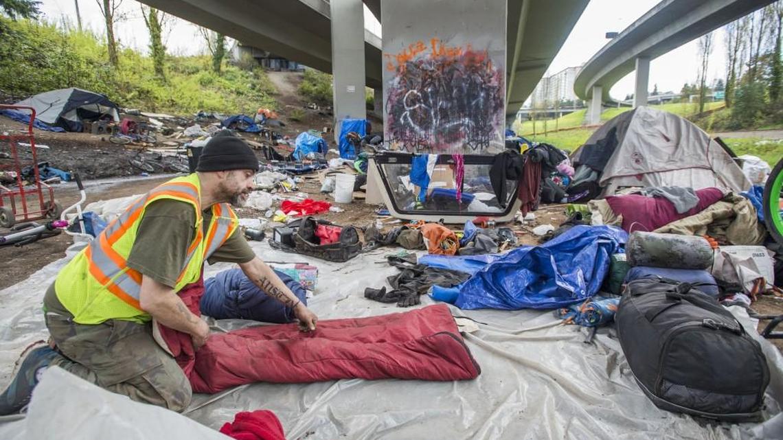 A local homeless man rolls up his sleeping bag while breaking down his tent site at a camp under the Interstate 705 overpass closed by city and state officials in Tacoma last year.