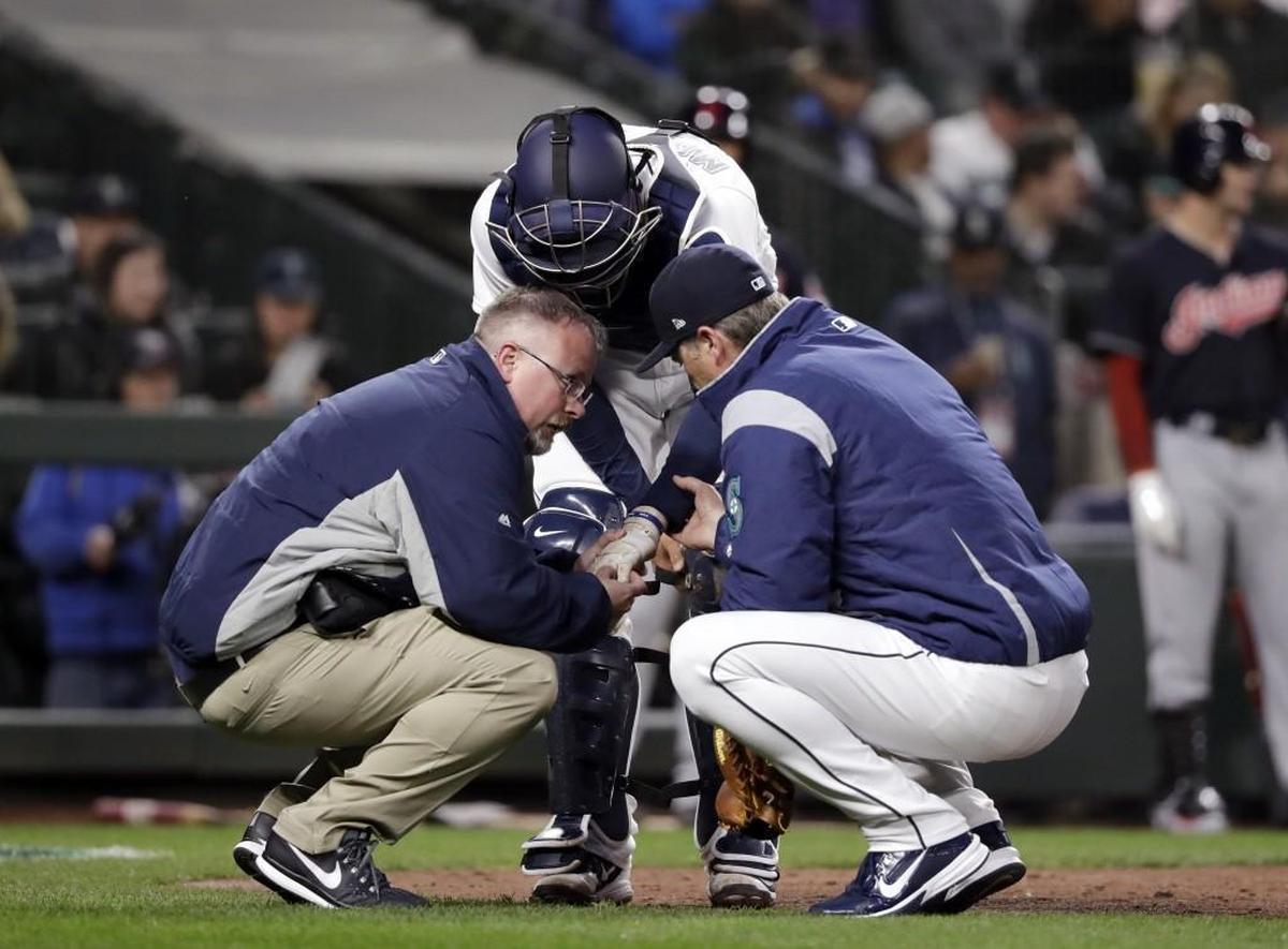 Seattle Mariners catcher Mike Marjama is examined by a trainer and manager Scott Servais, right, after Marjama was injured against the Cleveland Indians in a baseball game Thursday, March 29, 2018, in Seattle. The catcher remained in the game. (AP Photo/Elaine Thompson)