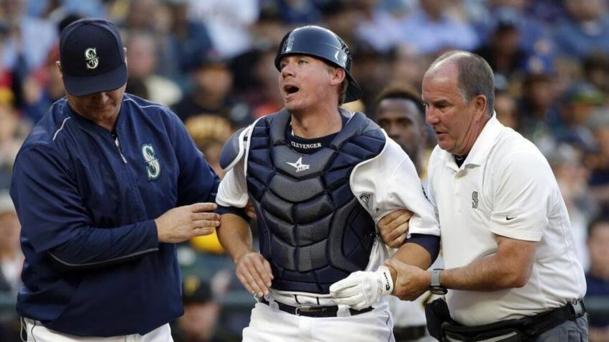 Seattle Mariners catcher Steve Clevenger, center, is helped to his feet by manager Scott Servais, left, and trainer Rick Griffin in 2016. Griffin, who has been with the team for 35 years, is retiring from day-to-day duties.