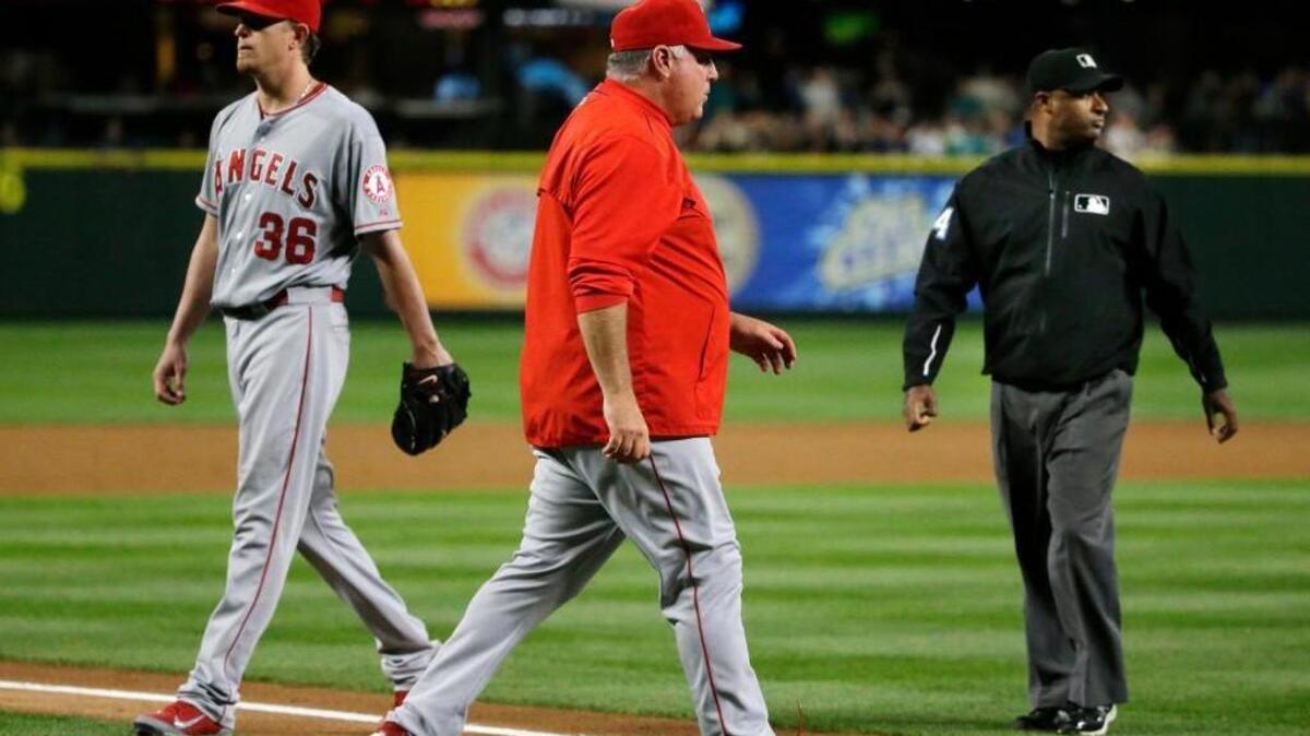 
Angels starting pitcher Jered Weaver, left, walks off the field as manager Mike Scioscia, center, walks out to talk to home plate umpire Brian O’Nora, not seen, after O’Nora ejected Weaver from for hitting the Mariners’ Kyle Seager with a pitch in the fifth inning Wednesday.
