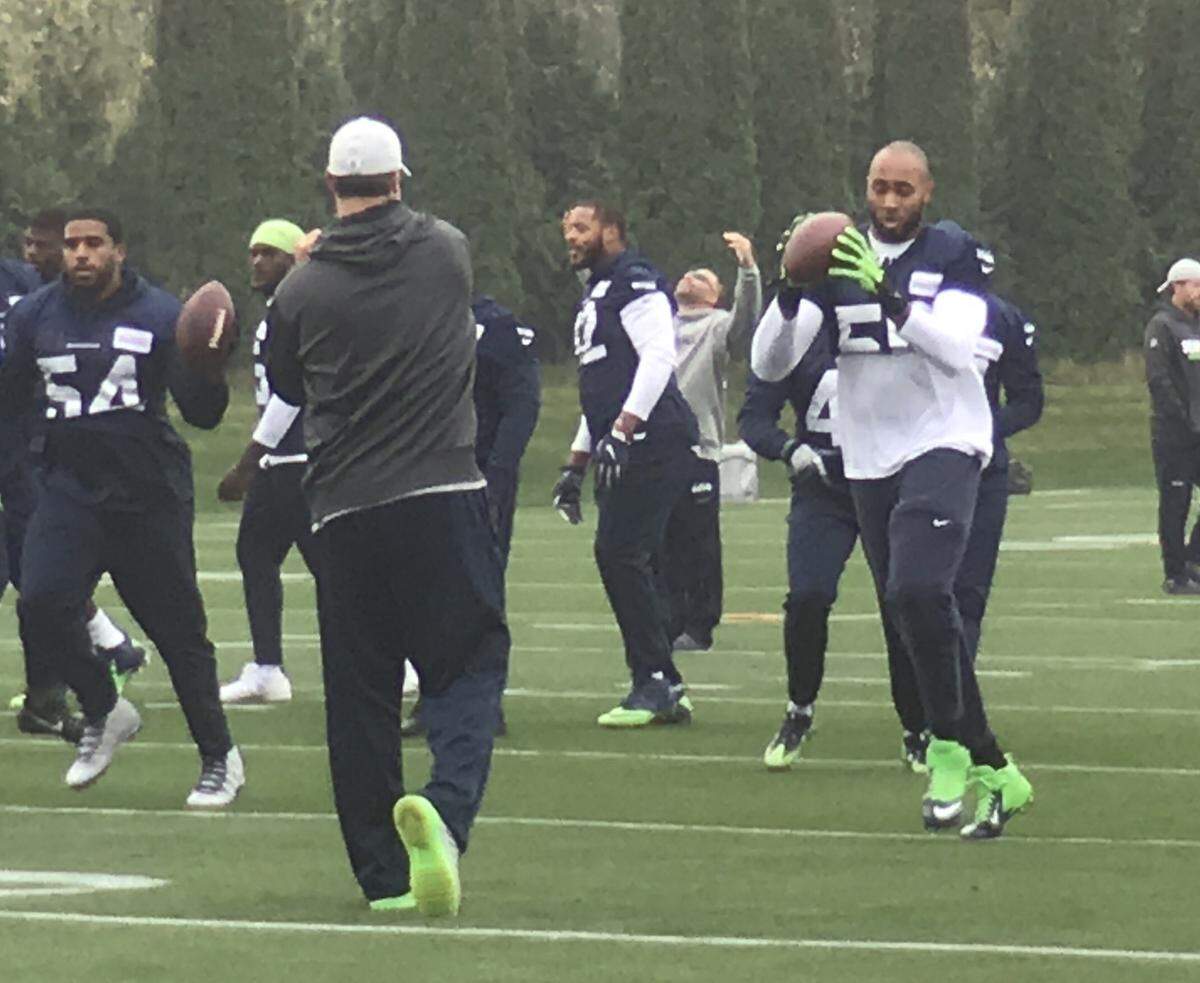 K.J. Wright (right, green gloves) catches a pass from a Seahawks assistant at the start of practice Monday at team headquarters in Renton. It was Wright’s first time on the field participating since his arthroscopic knee surgery in late August. The Pro Bowl outside linebacker is on track to make his season debut Sunday at Detroit.