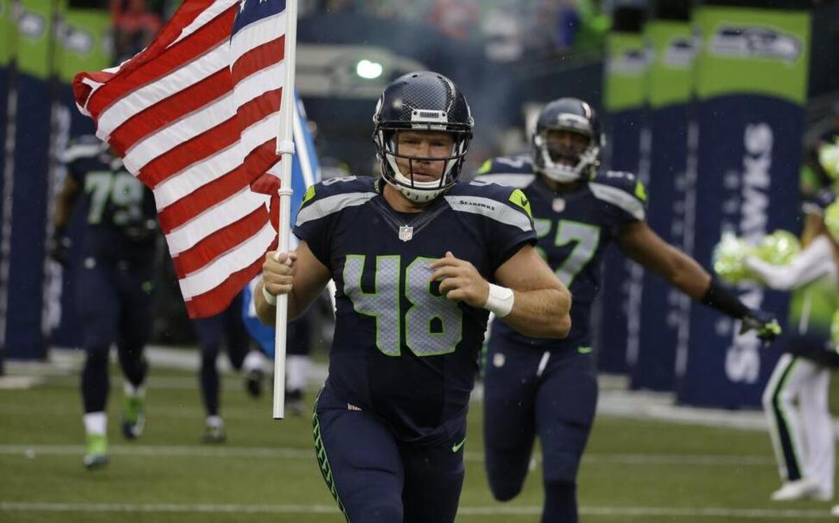 
Former Seahawks long snapper and military veteran Nate Boyer runs out of the tunnel Friday at CenturyLink Field with an American flag before the team’s exhibition opener against the Denver Broncos. Boyer was released by the Seahawks on Tuesday to make way for quarterback Jake Waters.
