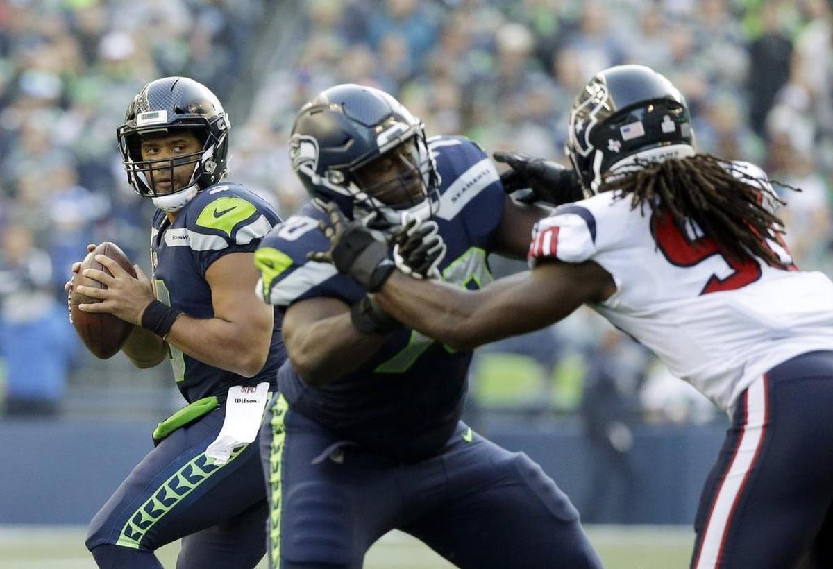 Seahawks quarterback Russell Wilson, left, drops to pass behind the blocking of left tackle Rees Odhiambo, center, against Houston Texans pass rusher Jadeveon Clowney Sunday. A league source confirmed Tuesday to The News Tribune that Wilson restructured his contract so the Seahawks can get a new left tackle in a trade with the Texans: three-time Pro Bowl blocker Duane Brown.