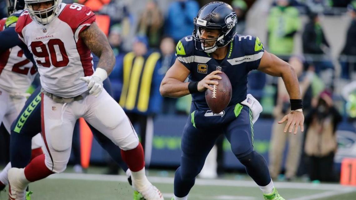 Seattle Seahawks quarterback Russell Wilson, right, scrambles away from Arizona Cardinals defensive tackle Robert Nkemdiche (90) during the first half Sunday in Seattle.