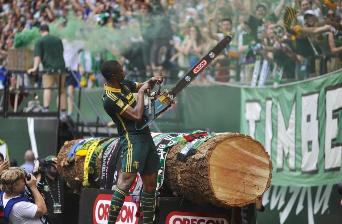 Portland Timbers'  Fanendo Adi (9) celebrates his goal by jumping the fence and holding up the chainsaw for the fans during the second half of an MLS Soccer game in Portland, Ore., Sunday June 28, 2015.  Portland beat Seattle 4-1. (AP Photo/Greg Wahl-Stephens)