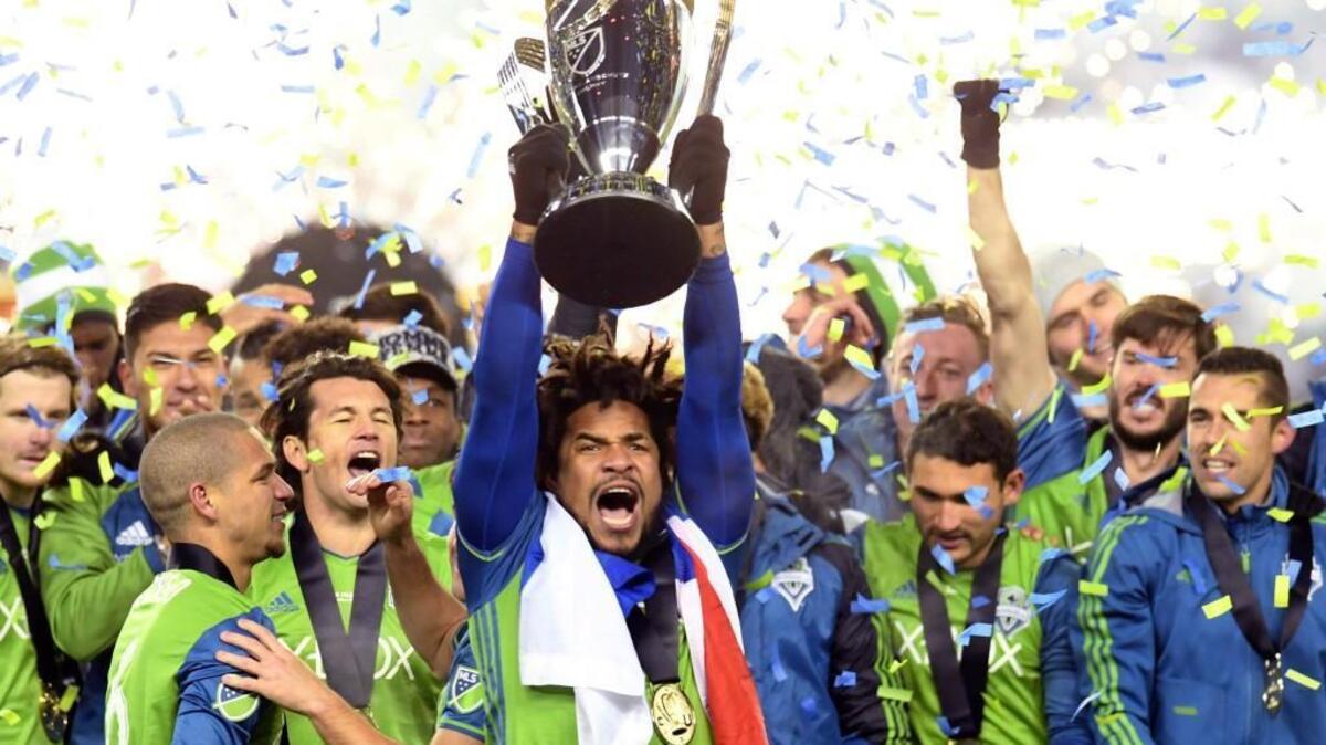 The Sounders’ Roman Torres, center, hoists the trophy while surrounded by his teammates after Seattle won the MLS Cup final in Toronto on Saturday night. Torres scored the decisive penalty kick after Toronto’s Justin Morrow hit his shot off the crossbar.