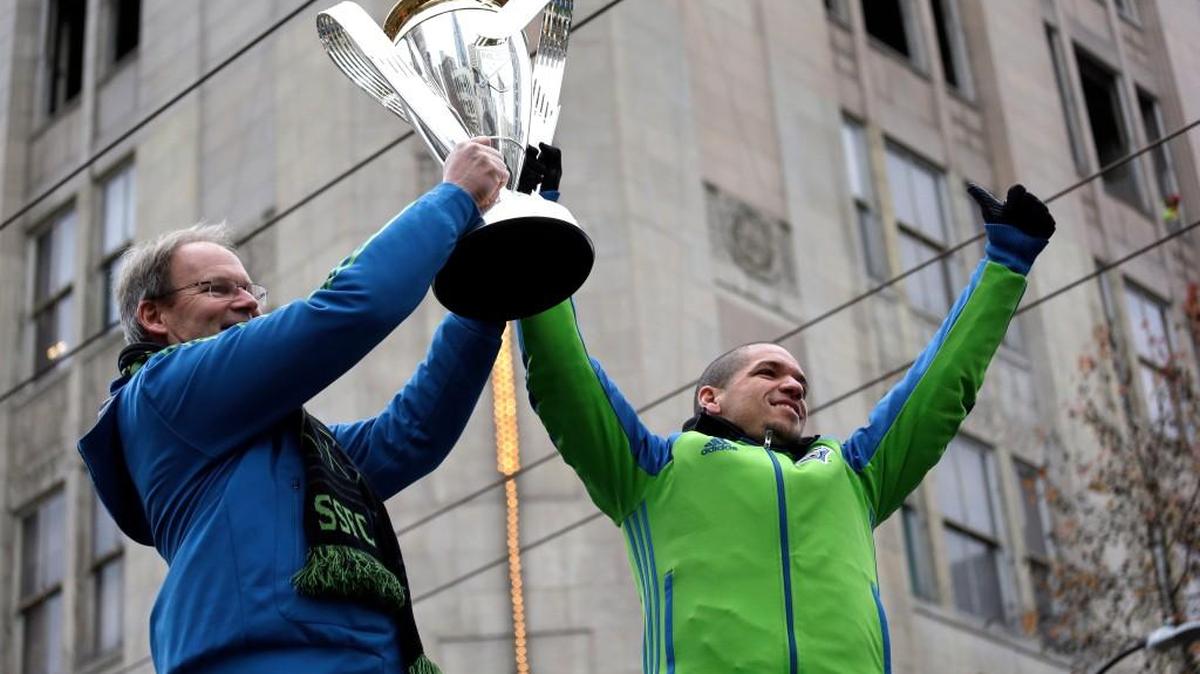 Seattle Sounders coach Brian Schmetzer, left, and midfielder Osvaldo Alonso heft the championship trophy before a march and rally Tuesday in Seattle celebrating the team’s MLS Cup Championship. Seattle beat Toronto FC 5-4 in a penalty kick shootout Saturday to win their first MLS championship.