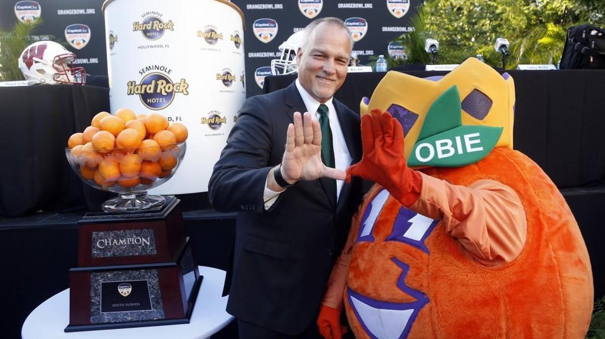 That’s no kind of mascot. Ask the Orange Bowl’s mascot, Obie, who is posing with Miami head coach Mark Richt, if he can operate a rider mower.